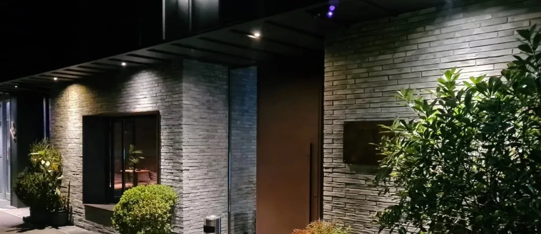Aangelichte gevel met Valrigo langformaten bij avond, met scherpe horizontale schaduwlijnen